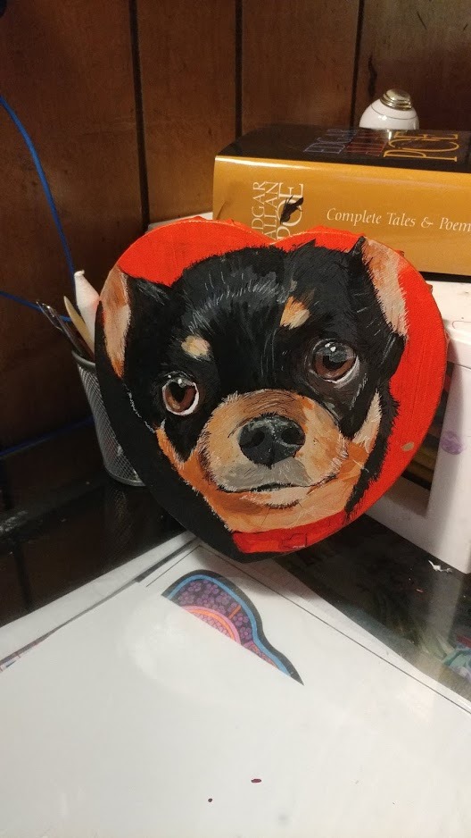 A black and break chihuahua on a heart shaped canvas with an orange background.